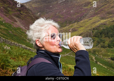 Soif active senior woman Walker de l'eau en bouteille de boisson une bouteille en plastique tandis que dehors la randonnée en plein air dans les montagnes du Nord du Pays de Galles Royaume-uni Grande-Bretagne Banque D'Images