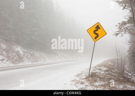 Un signe de route sur une route de montagne dans la neige et le brouillard. Banque D'Images