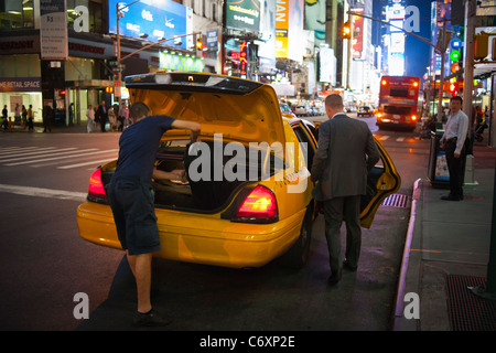 Un voyageur entre dans une cabine, comme le chauffeur de taxi charge ses bagages dans un taxi à Times Square à New York Banque D'Images