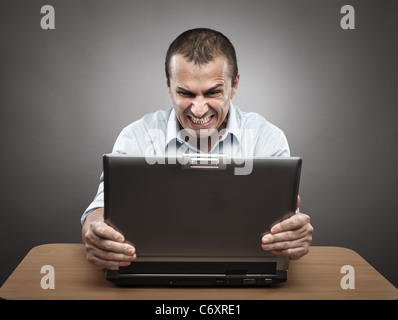 Portrait d'un homme en colère à son ordinateur portable, sur fond gris Banque D'Images