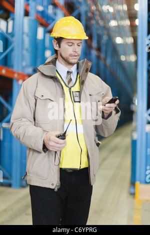 Travailleur using cell phone in warehouse Banque D'Images
