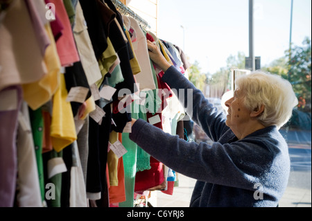 Une vieille dame à la recherche à travers les vêtements dans le St Luke's hospice charity shop dans le district londonien de Harrow Banque D'Images