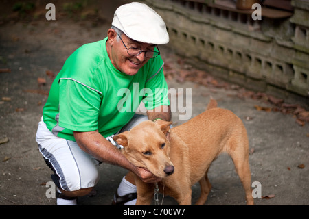 Un vieil homme hispanique Senior citizen de flatter son chien avec un grand sourire sur son visage. Banque D'Images