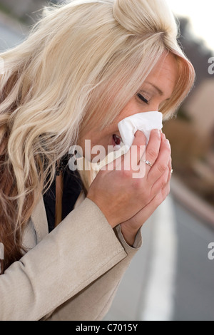 Cette jeune femme d'éternuer dans un mouchoir, soit a un rhume ou allergies vraiment mauvais. Banque D'Images