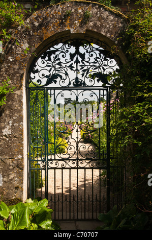 La porte en fer forgé ouvragé situé dans une arche en pierre de Cotswold mène à le jardin clos de Rousham House dans l'Oxfordshire, Angleterre Banque D'Images