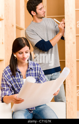 Amélioration de l'heureux jeune couple avec des plans d'architecture maison fixation Banque D'Images