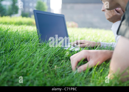 Les personnes qui utilisent un ordinateur portable en position allongée sur l'herbe, cropped Banque D'Images