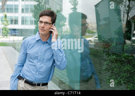 Libre de appuyé contre mur de verre, talking on cell phone Banque D'Images