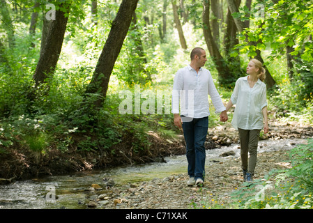 Couple walking par cours d'eau à travers les bois Banque D'Images