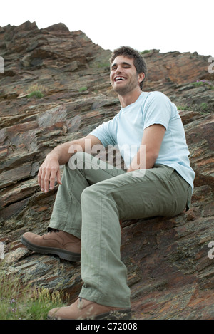 Man laughing while sitting on rock, low angle view Banque D'Images