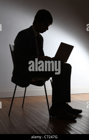 Silhouette d'un jeune homme en costume, assis à l'aide d'un ordinateur portable. Banque D'Images