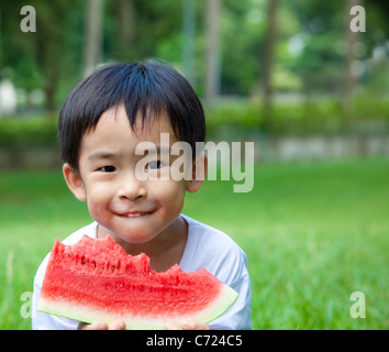 Cute asian boy eating watermelon sur l'herbe Banque D'Images