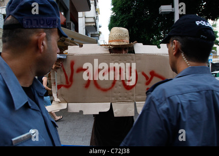 Les policiers israéliens observent alors qu'un manifestant tient un écriteau indiquant « la police est mauvaise » lors d'une manifestation contre la police qui a arrêté 40 manifestants lors d'un affrontement violent la semaine dernière. La précédente manifestation était en réponse à la tentative de la municipalité d’évacuer les villes de tentes établies dans différents quartiers en juillet. 40 manifestants ont été arrêtés avec force. Banque D'Images