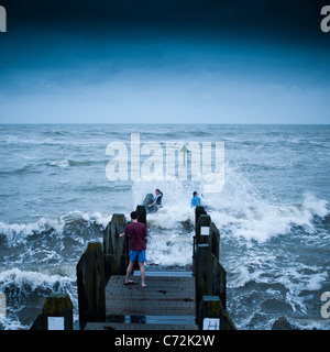 Au péril de leur vie - trois jeunes gens en esquivant les vagues que les tempêtes frappé Aberystwyth, sur la côte ouest du pays de Galles. Sept 11 2011 Banque D'Images