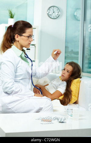 Portrait de clinicien dans les lunettes à la recherche au thermomètre avec sick girl situées près de par Banque D'Images