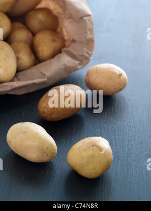 Pommes de terre grelots blancs s'échappant du sac brun sur fond sombre Banque D'Images