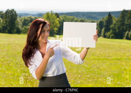 Young businesswoman sunny meadow pointant de côté au bandeau publicitaire vierge Banque D'Images