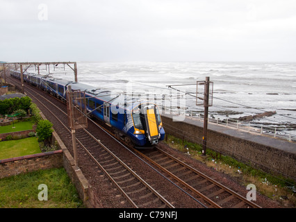 Un British Rail Class 380 train approchant Saltcoats avec une mer agitée à l'arrière-plan. Banque D'Images