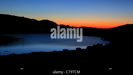 Avant le lever du soleil le ciel soit rougeâtre sur un lac alpin Banque D'Images