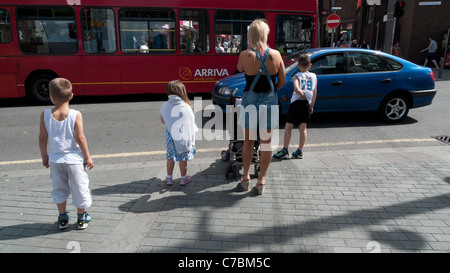 Vue arrière de l'attente de la famille à cross road sur une rue de ville avec voiture & bus arriva dans la circulation Walthamstow High Street à Londres Angleterre Royaume-uni KATHY DEWITT Banque D'Images