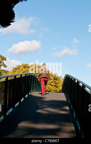 Femme en pantalon rouge traversant le pont piétonnier de l'anguille l'île Pie, Twickenham, Middlesex, England, United Kingdom Banque D'Images