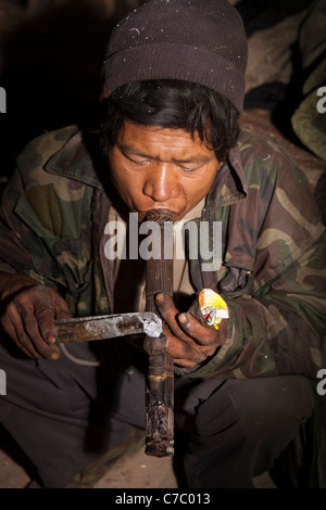 L'Inde, Nagaland, Longwa, Opium Den, Naga Konyak appliquant l'homme à la lumière du tuyau d'opium ember Banque D'Images