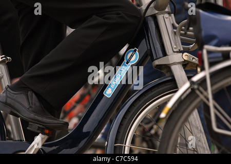 La jambe d'un homme d'affaires sur un Boris Bike en attente avec d'autres cyclistes de traverser une route Banque D'Images