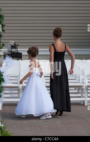 Fleur fille avec une autre jeune fille invité de mariage devant des rangées de chaises blanches mis en place pour le mariage en plein air haute résolution Banque D'Images