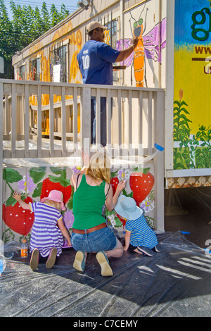 Un jeune bénévole des femmes et ses filles peinture décorations sur un bâtiment de ville au cours d'un programme d'embellissement de la collectivité. Banque D'Images