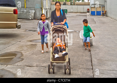 Une jeune mère hispanique et ses trois enfants transporter accueil aliments donnés à un organisme de bienfaisance la distribution à Santa Ana, CA. Banque D'Images