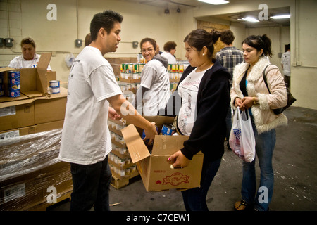 Les Hispaniques et les volontaires Caucasiens donnent de la nourriture à une jeune femme à une distribution alimentaire de bienfaisance à Santa Ana, CA. Banque D'Images