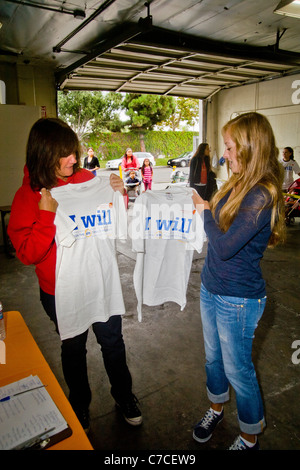 Deux nouvelles femmes bénévoles, obtenez un logo T-shirts à un organisme de bienfaisance distribution gratuite de nourriture à un entrepôt à Santa Ana, CA. Banque D'Images