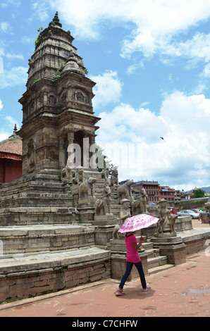 Une femme avec un parapluie passe devant une Inde-style temple building dans Durbar Square, Bhaktapur, près de Katmandou, Népal. Banque D'Images