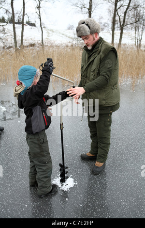 Un garçon pêche sur glace le forage d'un trou dans le lac Stora Bellen, Belloe, Suède Banque D'Images