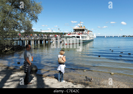 Les gens et le chien debout sur un estran Chiemsee Ferry dans la distance à l'Herreninsel, Chiemgau Haute-bavière Germa Banque D'Images