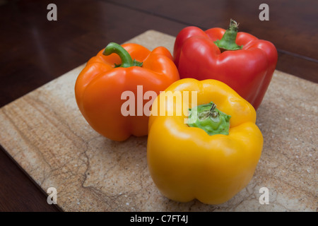 Trois poivrons ; orange, jaune et rouge sur la planche à découper en marbre Banque D'Images