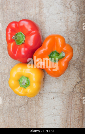 Vue d'ensemble de trois poivrons assis sur une planche à découper. Banque D'Images