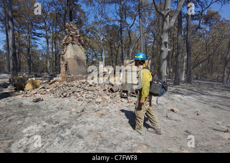 Le port de vêtements de sécurité pompier cherche les points chauds dans une zone résidentielle très boisés touchés par de forêt près de Brenham Texas Banque D'Images