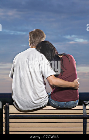 Un couple assis sur un banc, regardant le coucher de soleil Banque D'Images