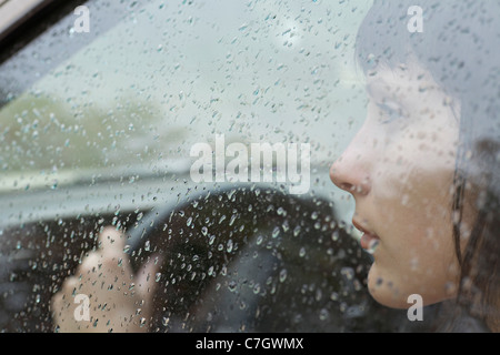 Une femme chauffeur sitting in car looking out window, gouttes sur la fenêtre Banque D'Images