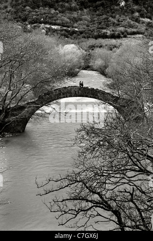 Un couple traversant le pont voûté en pierre, de Klidonia, sur la rivière Voidomatis, . L'Epire Ioannina, Grèce, (B&W) Banque D'Images