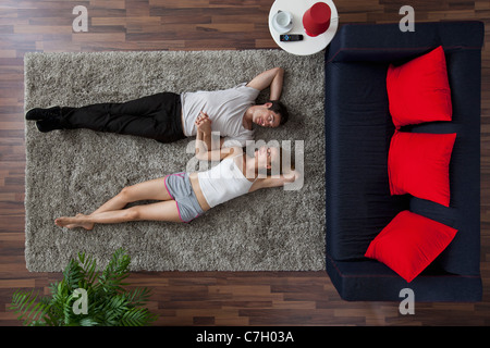 Un couple allongé sur un tapis de salon, se tenant la main et en regardant les autres, overhead view Banque D'Images