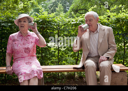 Man and Woman parler sur l'étain pouvez téléphones sur banc dans park Banque D'Images