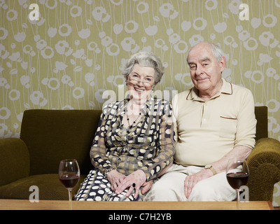 Mari et femme détendue sur canapé, avec deux verres de vin rouge sur la table en face Banque D'Images