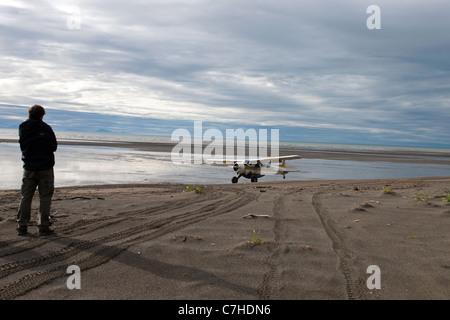 Un homme regarde un seul moteur prop avion atterrir sur une plage de sable fin, le lac Clark National Park, Alaska, United States of America Banque D'Images