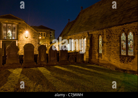 Extérieur de l'église en soirée et pierres de jardin (lumières allumées, vitraux lumineux et arbre de Noël décoré) - Baildon, Yorkshire, Angleterre. Banque D'Images