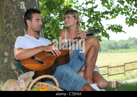 Jeune couple avec panier pique-nique assis par tree Banque D'Images