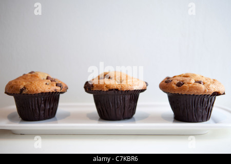 Trois muffins aux pépites de chocolat placées sur une longue plaque blanche Banque D'Images