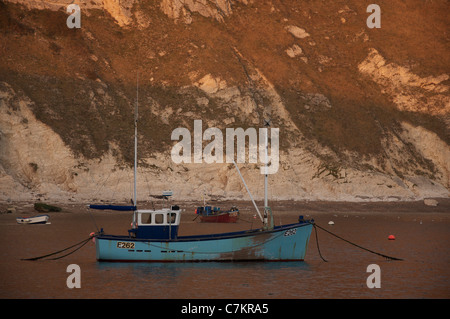 Un seul bateau de pêche amarré dans la crique de Lulworth Cove, avec de hautes falaises de craie dans l'arrière-plan. L'île de Purbeck, Dorset, Angleterre, Royaume-Uni. Banque D'Images