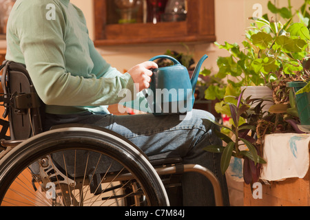 Femme avec la sclérose en plaques dans un fauteuil roulant d'arroser les plantes d'appartement Banque D'Images